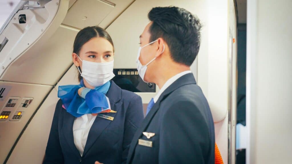 Airline pilot and cabin crew wearing protective masks discussing flight operations inside an aircraft cabin.
