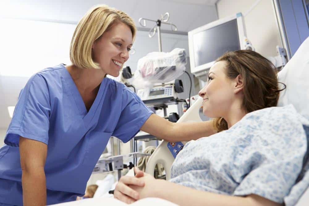 Nurse comforting a female patient recovering in a modern hospital room during medical treatment abroad.
